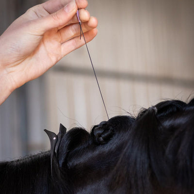 Image of someone threading Hairy Pony Flat Waxed Plaiting Thread through a black horse's mane.
